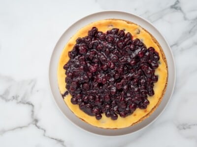 Fully chilled lemon blueberry cheesecake topped with glossy homemade blueberry sauce, served on a white plate.