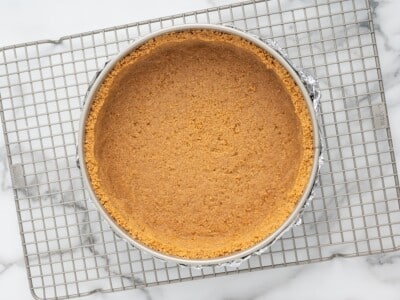 Baked graham cracker crust pressed into a foil-wrapped springform pan on a wire cooling rack.