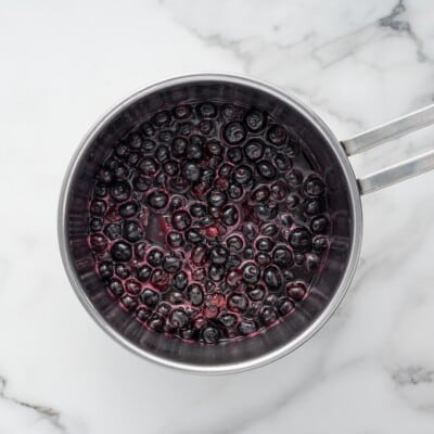 Fresh blueberries simmering in a saucepan with sugar, lemon juice, and water to make the blueberry topping.