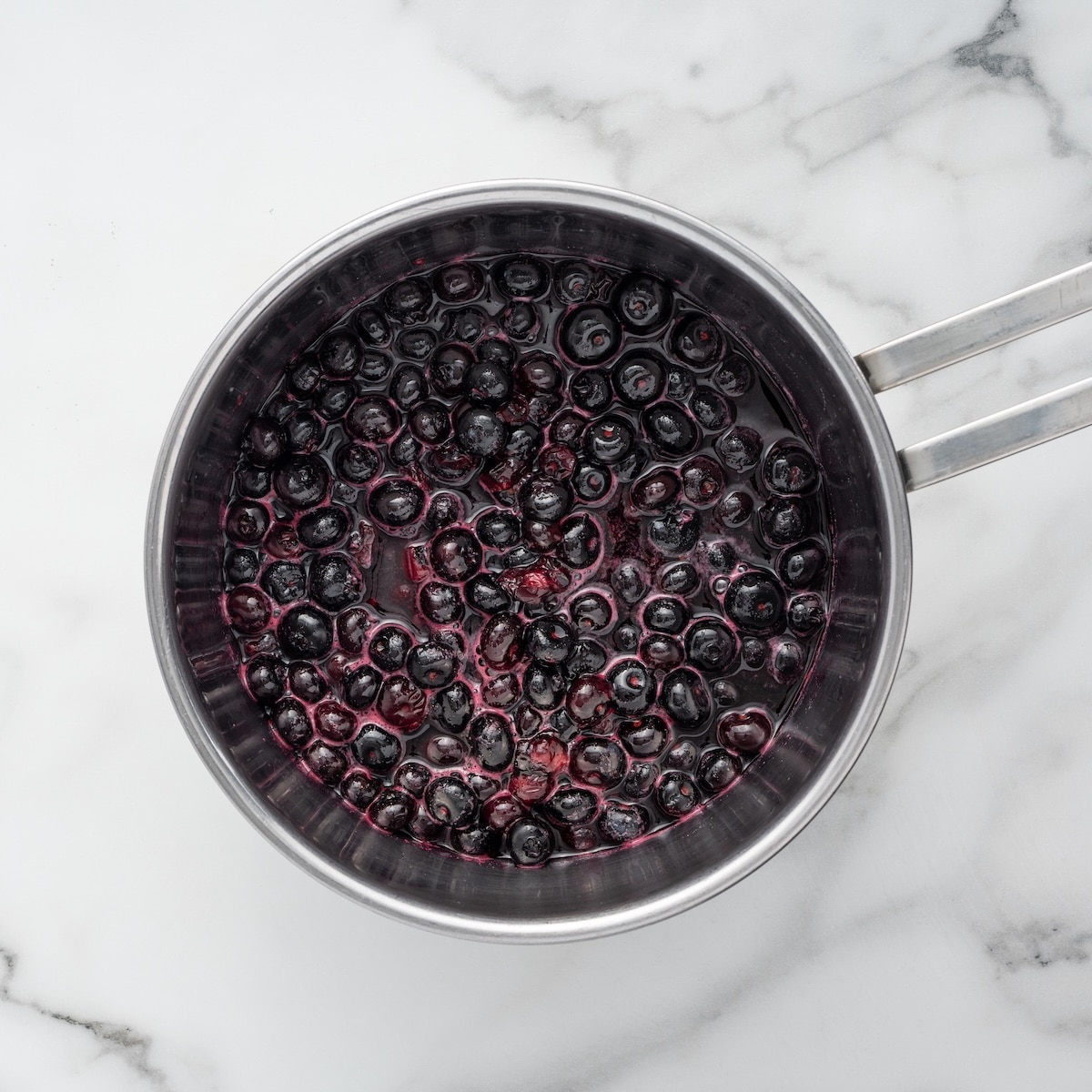 Fresh blueberries simmering in a saucepan with sugar, lemon juice, and water to make the blueberry topping.