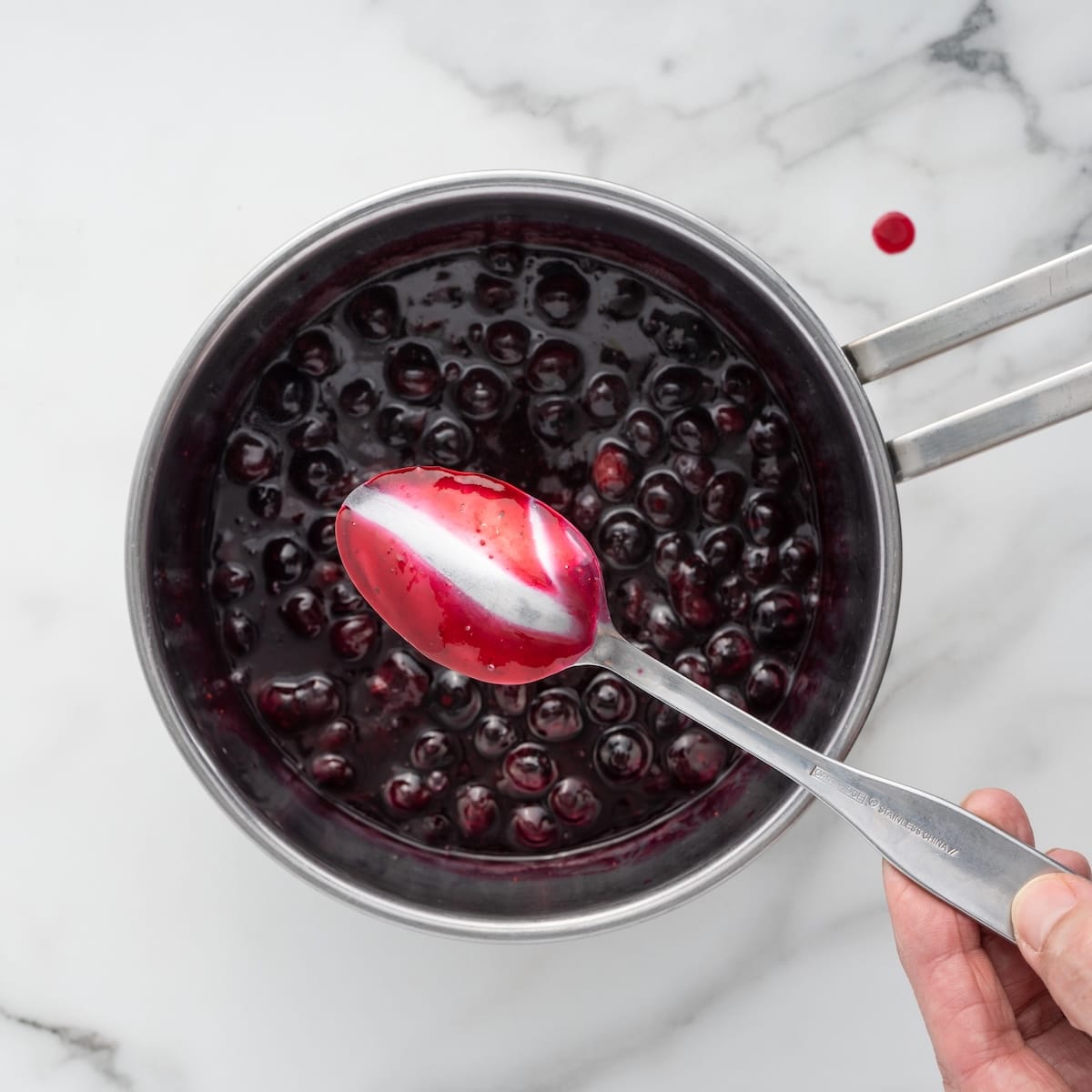 Thickened blueberry sauce coating the back of a spoon, showing the right consistency before removing from the heat.