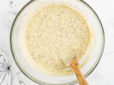 Finished lemon poppy seed bread batter in a glass mixing bowl with a wooden spoon