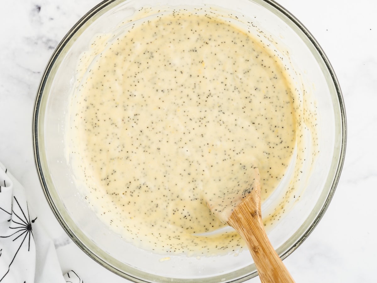 Finished lemon poppy seed bread batter in a glass mixing bowl with a wooden spoon