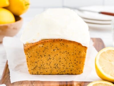 Lemon poppy seed bread loaf topped with thick white lemon glaze on a wood cutting board