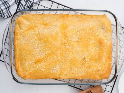 Fully baked sloppy joe bake in a glass dish on a wire cooling rack, top crust deep golden brown and scattered with sesame seeds.