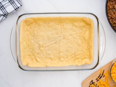 Pre-baked crescent roll dough lining the bottom of a glass 9x13 baking dish, light golden with seam lines still visible.