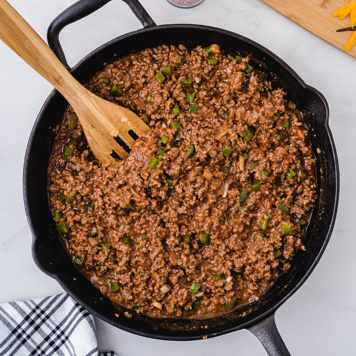 Sloppy joe filling simmering in a cast iron skillet, thick and glossy with visible pieces of green pepper throughout.