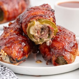 Two sliced Texas Twinkies on a white plate showing jalapenos filled with chopped brisket and cream cheese, wrapped in bacon and coated in barbecue sauce.