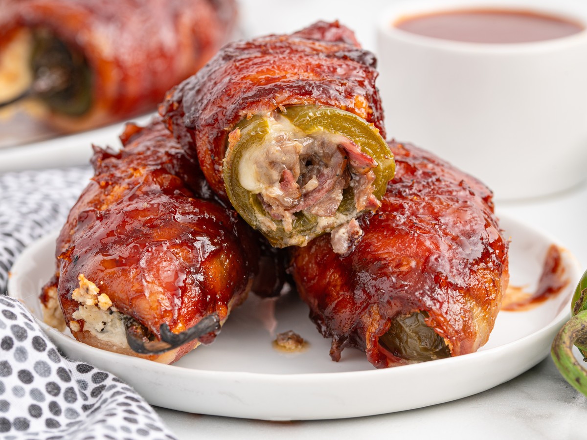 Two sliced Texas Twinkies on a white plate showing jalapenos filled with chopped brisket and cream cheese, wrapped in bacon and coated in barbecue sauce.