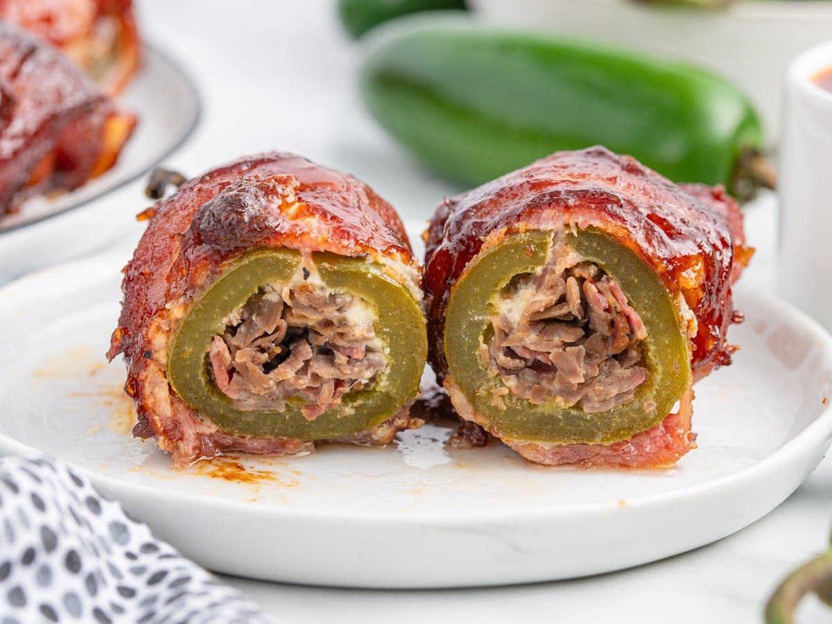 Close-up of Texas Twinkies cut in half with jalapenos stuffed with brisket, wrapped in bacon, and finished with sticky barbecue sauce.