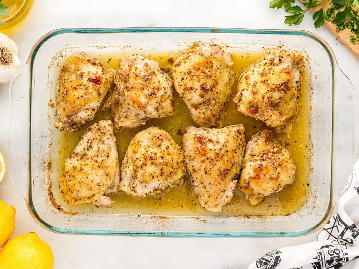 Baked chicken thighs in a glass dish before broiling, with golden skin and pan juices