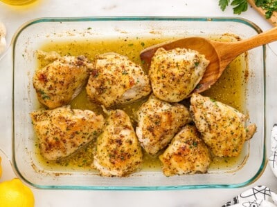 Crispy oven baked chicken thighs garnished with fresh parsley in a glass baking dish with a wooden spoon