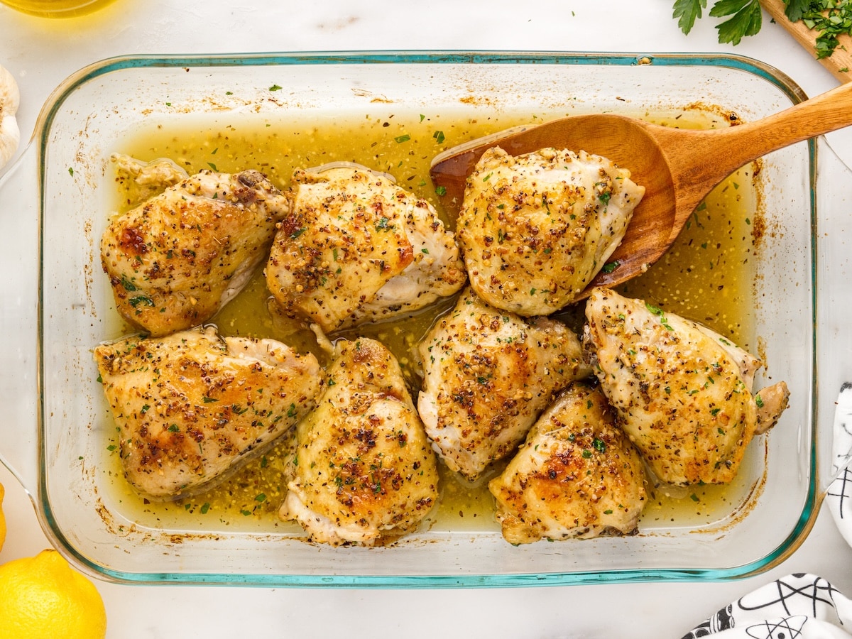 Crispy oven baked chicken thighs garnished with fresh parsley in a glass baking dish with a wooden spoon