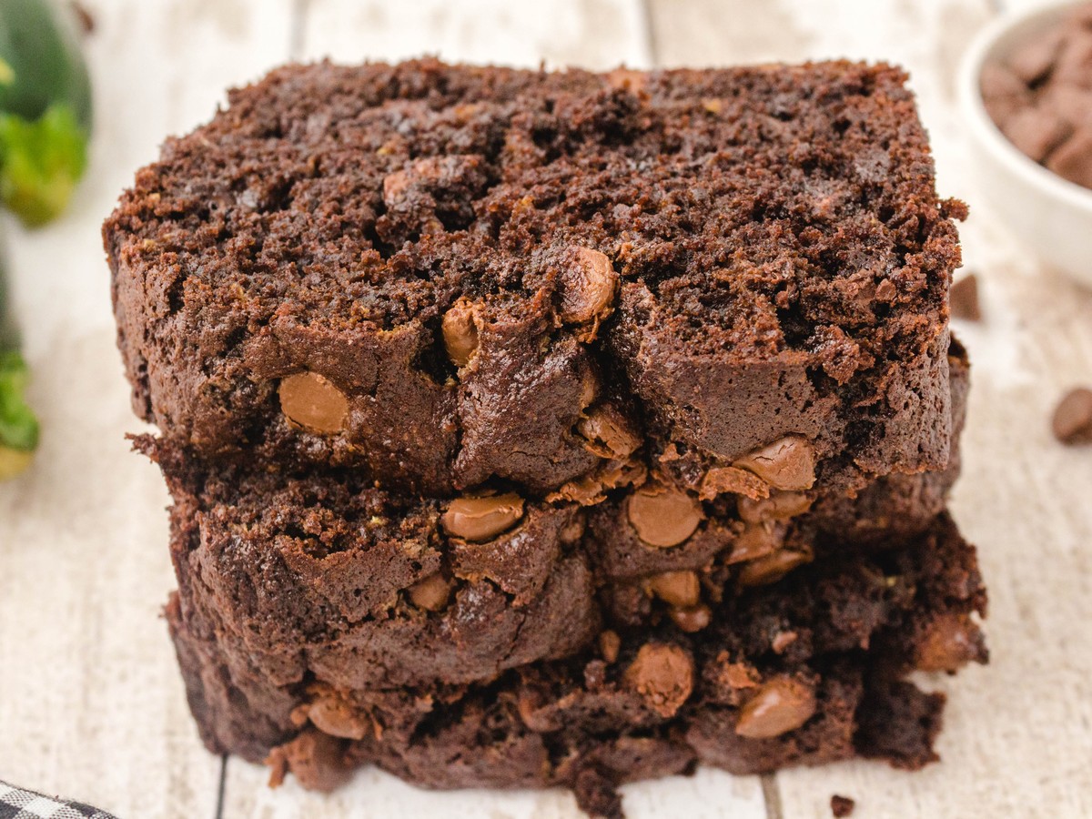 Stack of thick slices of moist Chocolate Zucchini Bread with melted chocolate chips and a rich, fudgy crumb on a rustic wooden surface.