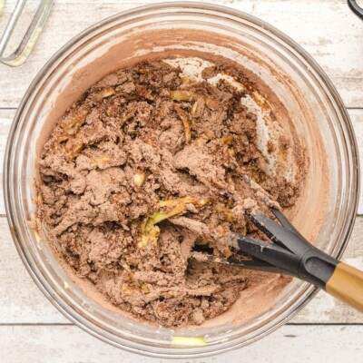 Overhead photo of the thick double chocolate zucchini bread batter after the dry ingredients have been added, showing shredded zucchini and cocoa mixture being folded together in a glass mixing bowl.