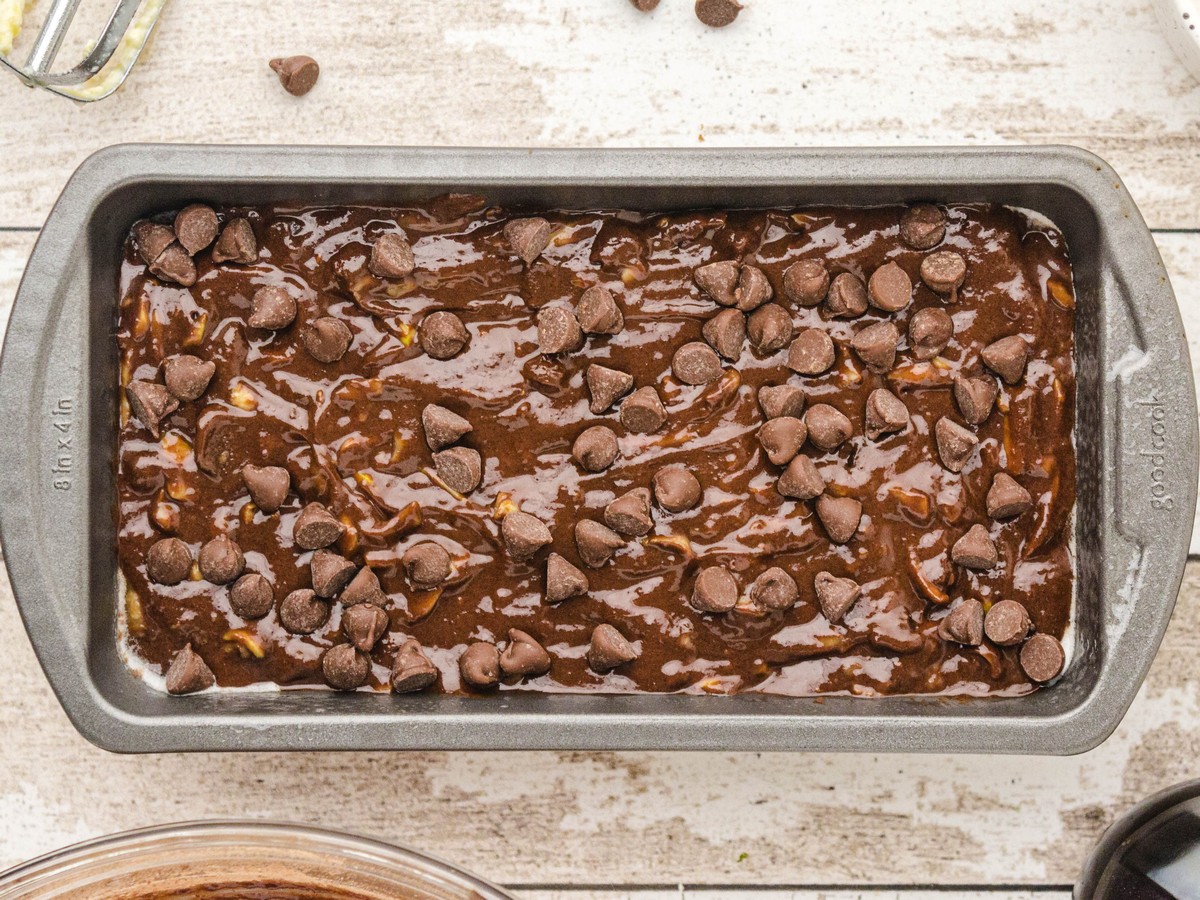 Overhead photo of chocolate zucchini bread batter spread into a loaf pan and topped with semi-sweet chocolate chips before baking.