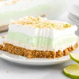 Layered Key Lime Pie Lasagna slice on a white plate with whipped topping, lime zest, creamy key lime filling, and a graham cracker crust.
