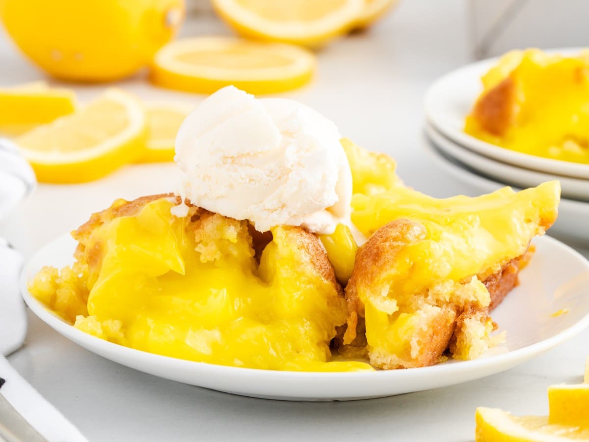 Warm Lemon Cobbler on a white plate with bright lemon filling, golden baked topping, and a scoop of vanilla ice cream, surrounded by fresh lemon slices.
