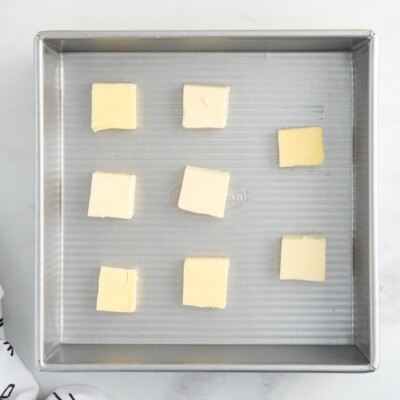 Cubes of salted butter arranged evenly in a square baking pan, the first step in preparing Lemon Cobbler before adding the lemon filling and batter.