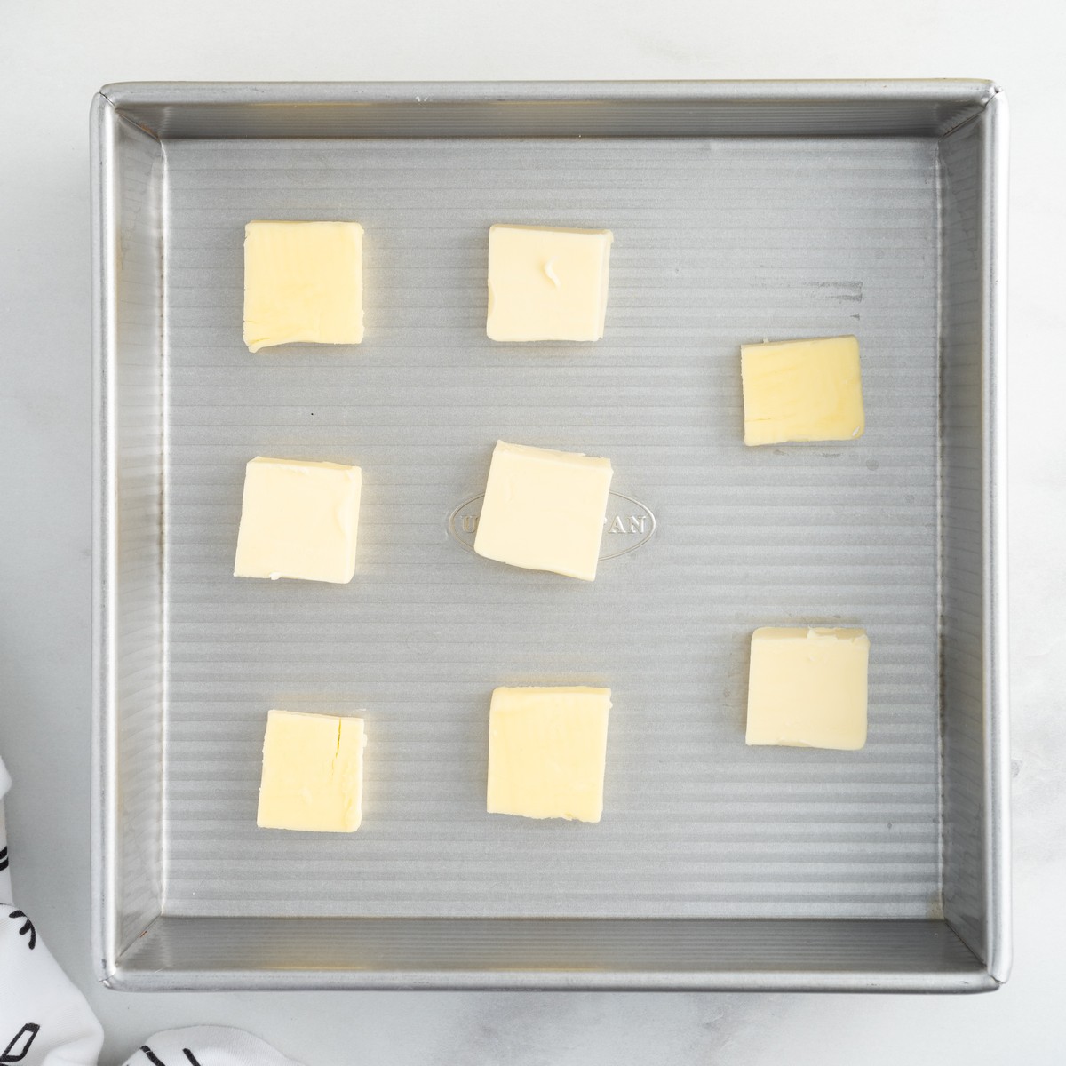Cubes of salted butter arranged evenly in a square baking pan, the first step in preparing Lemon Cobbler before adding the lemon filling and batter.