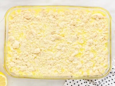Reserved cake mix dough crumbled over the lemon curd filling in a glass 9x13 baking dish, ready to bake.