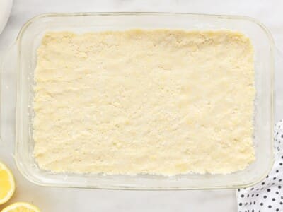Par-baked cake mix crust pressed into a glass 9x13 baking dish, with sliced lemons visible alongside.