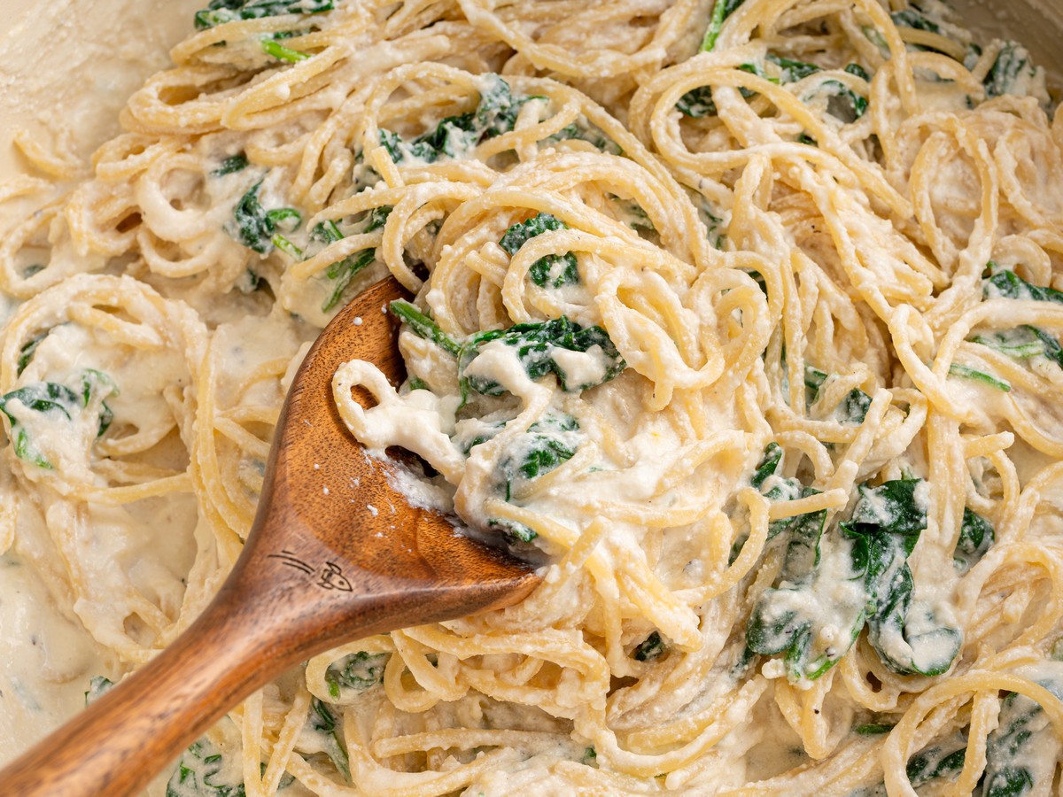 Close-up of Lemon Ricotta Pasta being served with a wooden spoon, showing spaghetti coated in creamy ricotta sauce with wilted spinach and a hint of lemon.