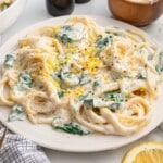 Creamy Lemon Ricotta Pasta served on a white plate, featuring spaghetti coated in a rich ricotta and parmesan sauce with tender spinach, fresh lemon zest, and cracked black pepper. Styled with lemon wedges and parmesan for a bright, easy pasta dinner.