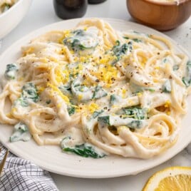Creamy Lemon Ricotta Pasta served on a white plate, featuring spaghetti coated in a rich ricotta and parmesan sauce with tender spinach, fresh lemon zest, and cracked black pepper. Styled with lemon wedges and parmesan for a bright, easy pasta dinner.