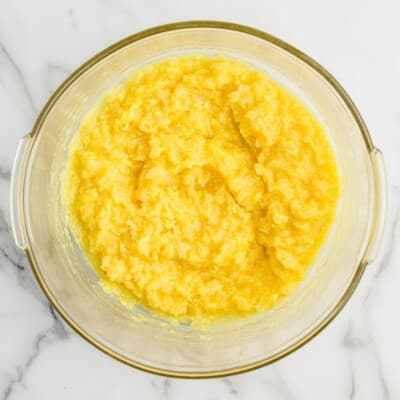 Overhead photo of crushed pineapple mixed with vanilla instant pudding in a glass bowl, creating the creamy yellow base for Pineapple Fluff dessert salad.