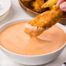 Crispy chicken tender dipped into creamy Red Robin Campfire Sauce in a white bowl.