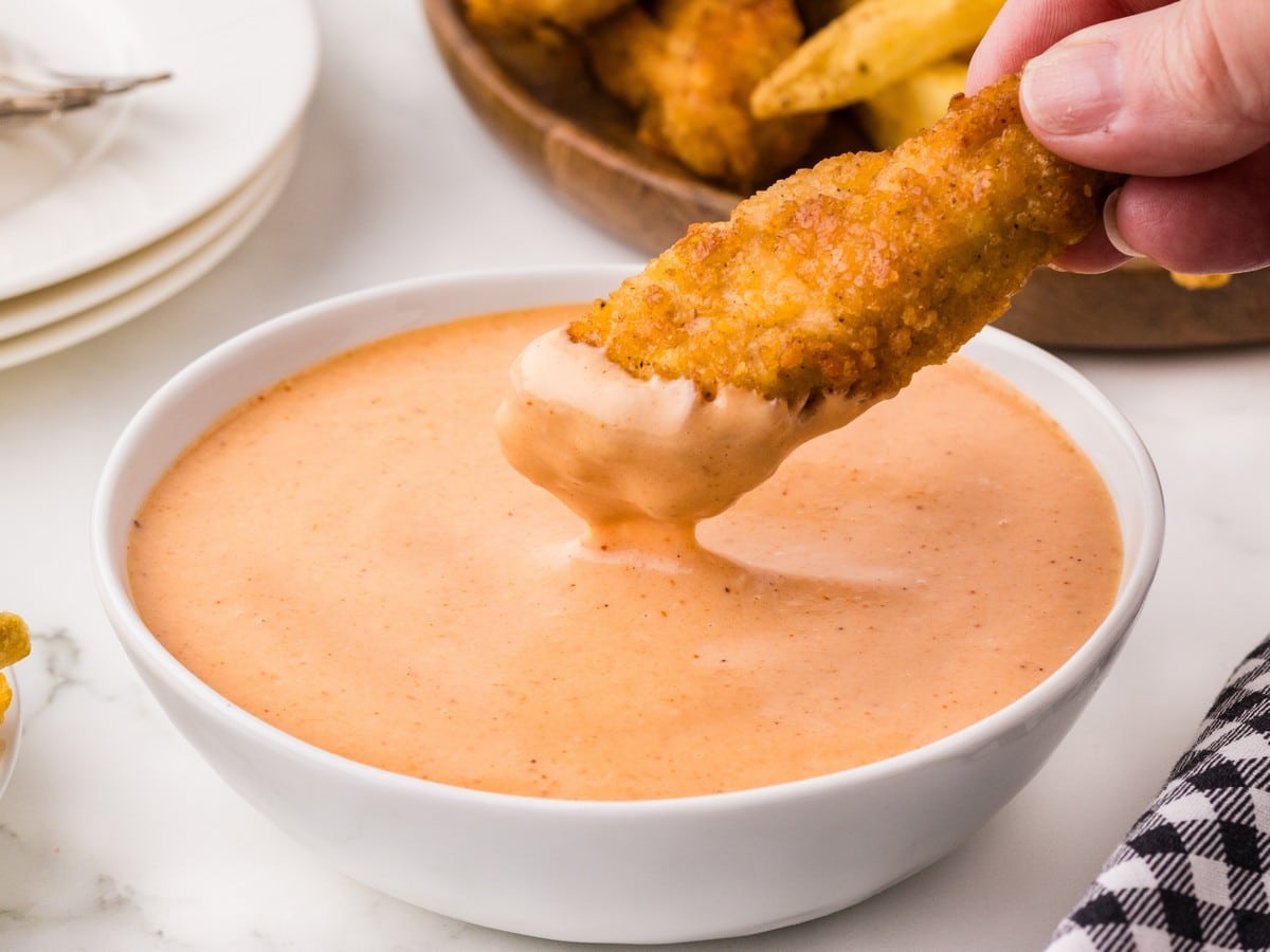 Crispy chicken tender dipped into creamy Red Robin Campfire Sauce in a white bowl.