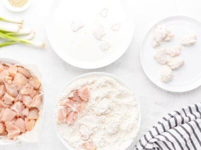 Diced chicken breast being coated in seasoned flour as part of the buttermilk double-dredge process for crispy sesame chicken.