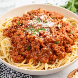 Close-up of classic Bolognese sauce spooned over spaghetti and finished with grated Parmesan and chopped parsley, highlighting the rich, meaty tomato sauce texture.