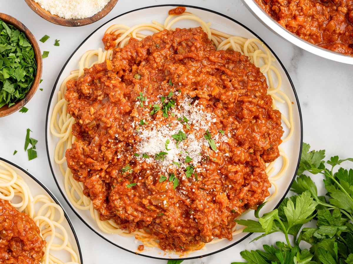 Overhead view of homemade Bolognese served over spaghetti, generously topped with Parmesan cheese and fresh parsley for a hearty Italian pasta dinner.