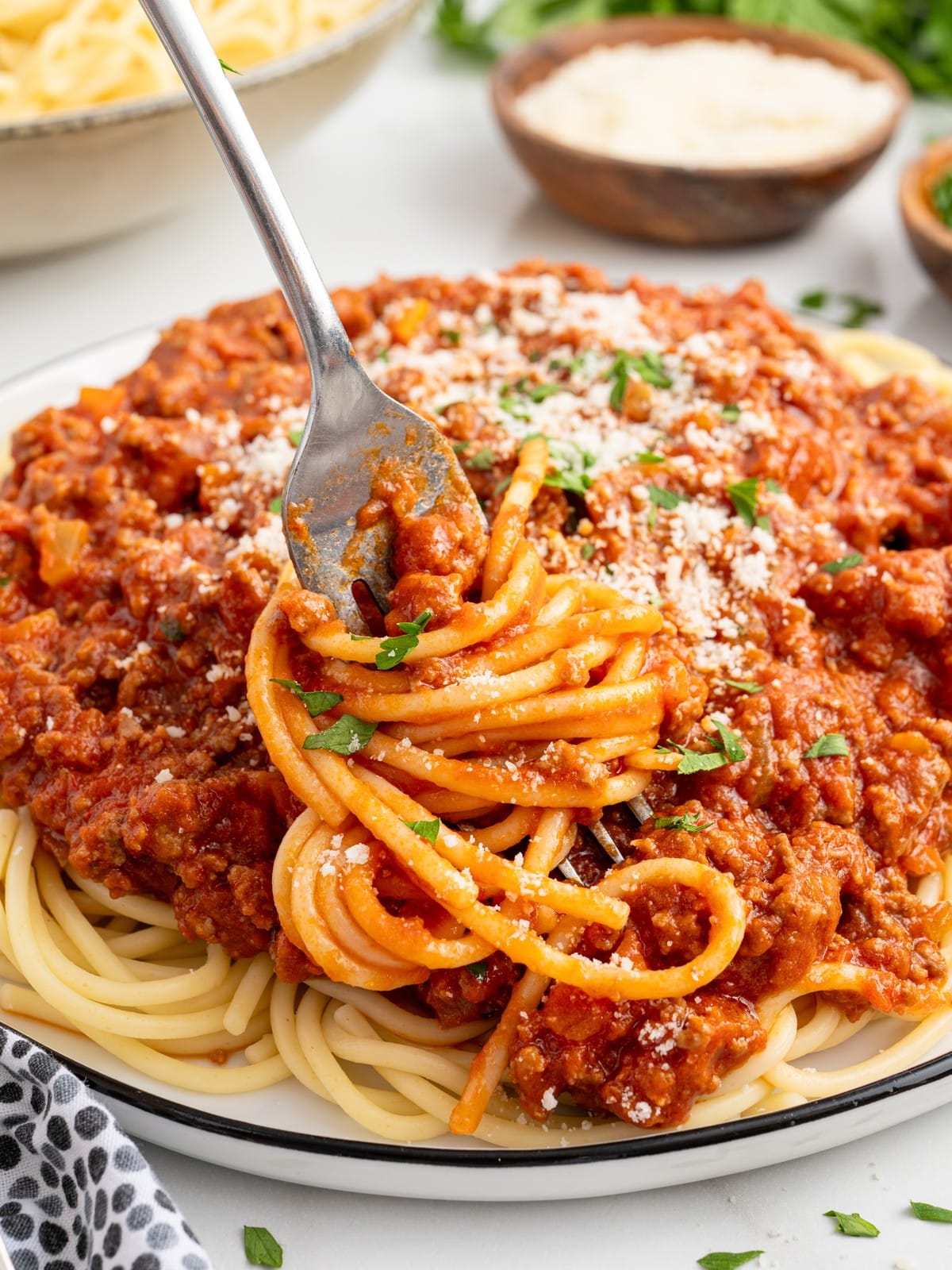 Fork twirling spaghetti coated in hearty homemade Bolognese sauce, finished with Parmesan cheese and fresh parsley, highlighting the thick, meaty texture of this classic pasta recipe.