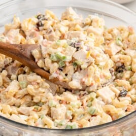Creamy Chicken Macaroni Salad mixed in a glass bowl with elbow macaroni, chicken, pineapple, celery, carrots, red onion, raisins, and cheddar cheese.