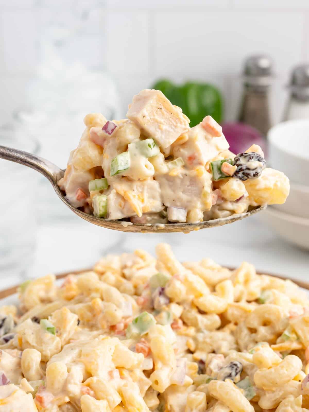 Spoonful of Chicken Macaroni Salad featuring tender chicken, elbow macaroni, pineapple, celery, carrots, red onion, raisins, and cheddar cheese coated in a creamy dressing.