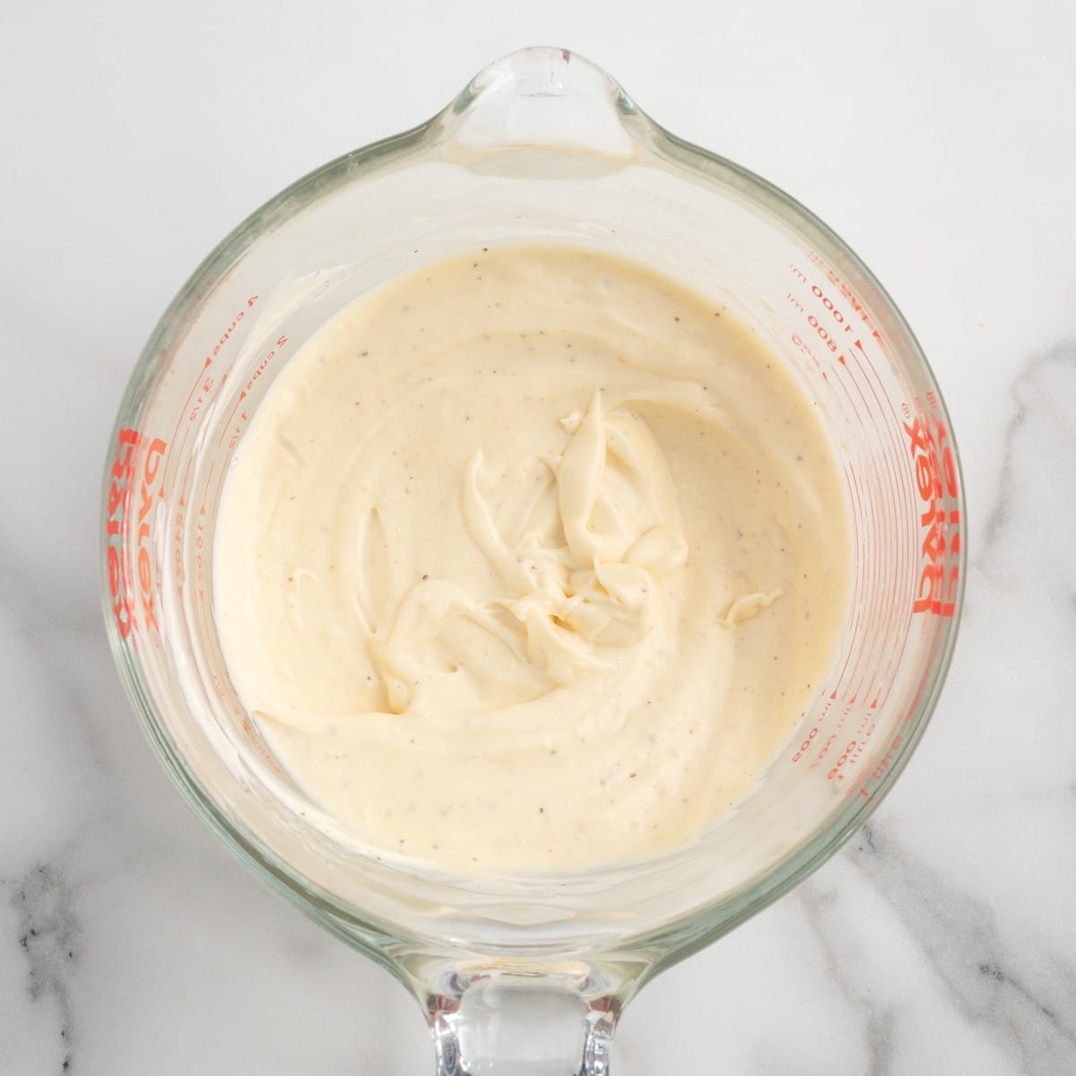 Creamy homemade dressing for Chicken Macaroni Salad mixed in a glass measuring cup, showing a smooth mayonnaise-based dressing seasoned and ready to coat the pasta salad ingredients.