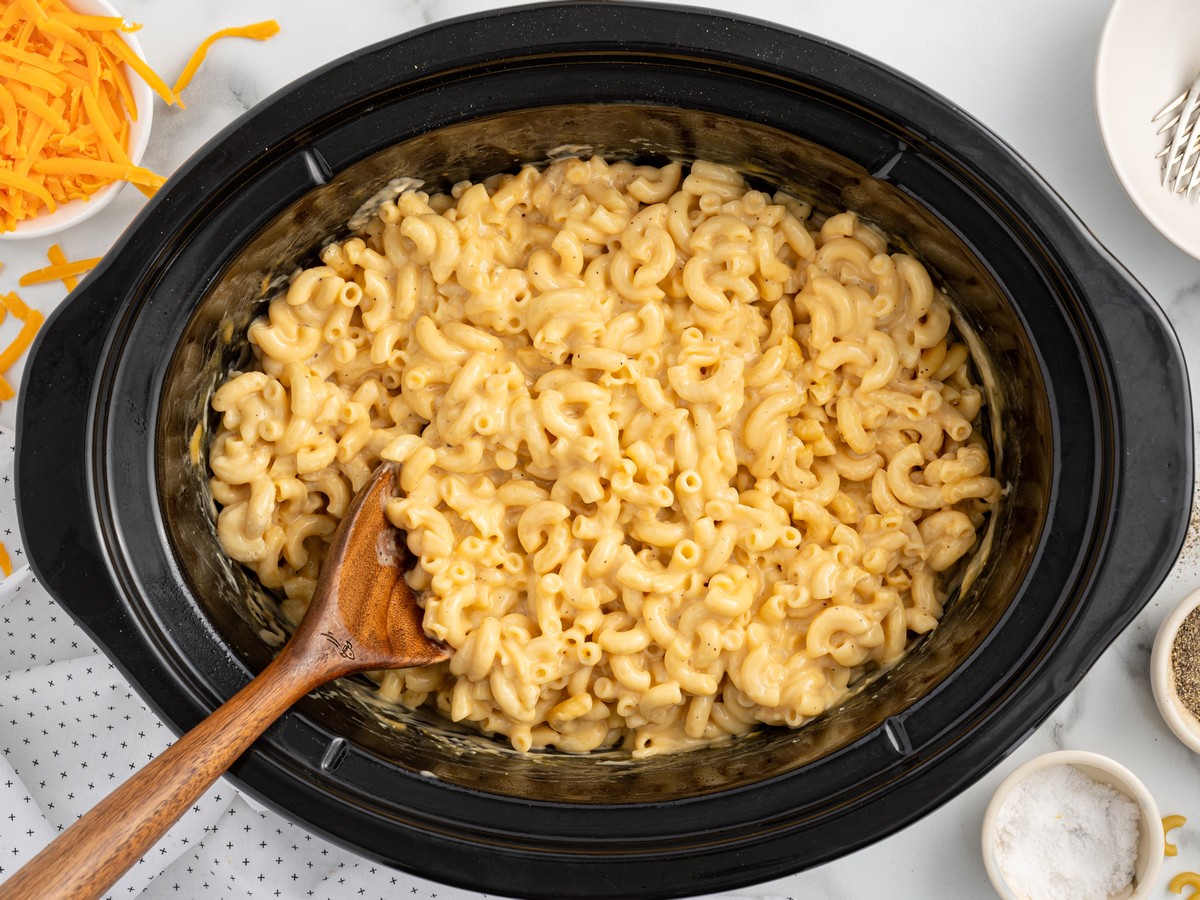 Overhead photo of creamy Crockpot Velveeta Mac and Cheese in a black slow cooker with elbow macaroni coated in smooth cheese sauce and a wooden spoon.
