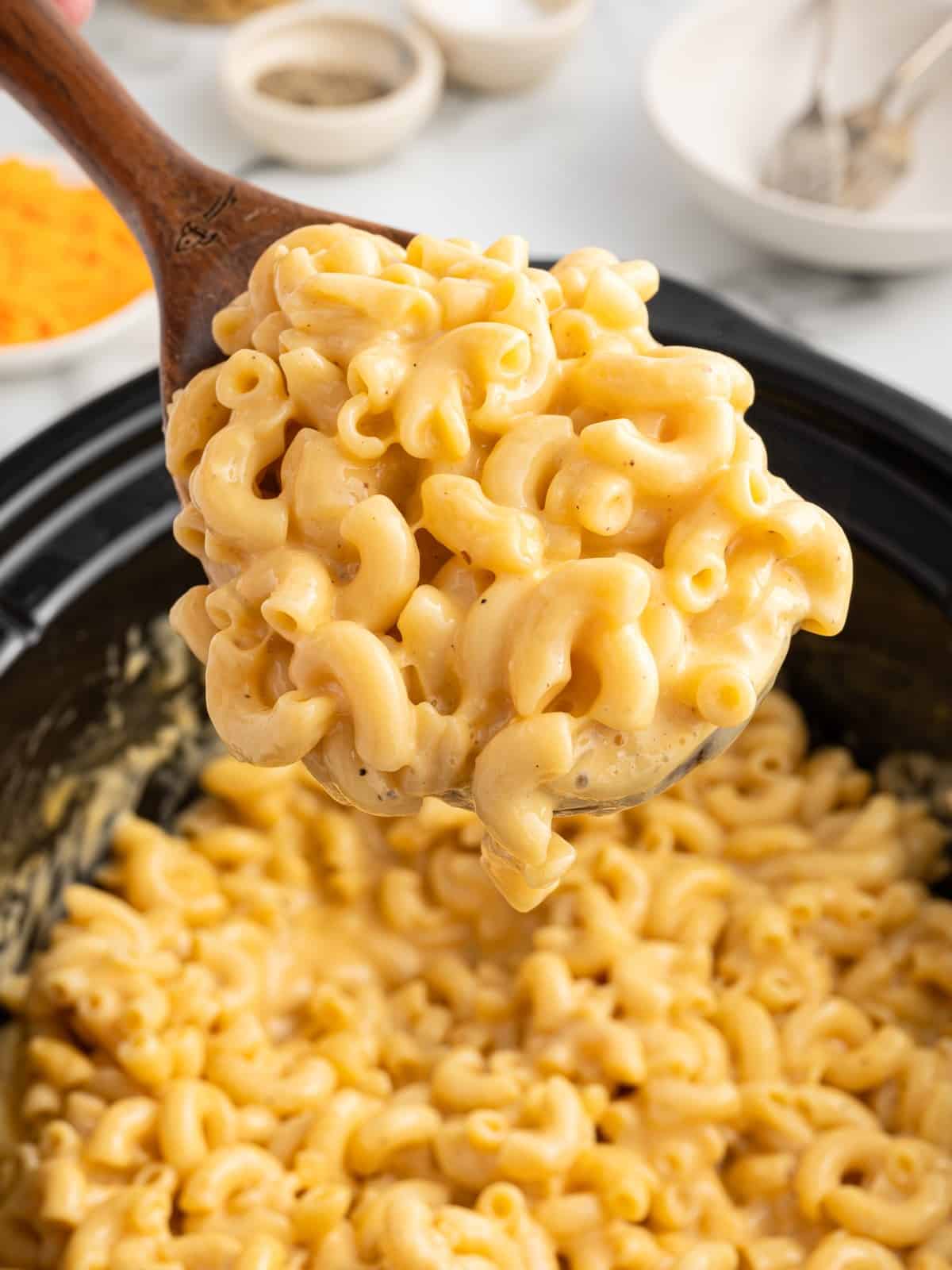 Wooden spoon lifting a serving of creamy Crockpot Velveeta Mac and Cheese with tender elbow macaroni coated in rich, cheesy sauce.