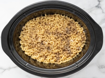 Overhead photo of cooked elbow macaroni in a slow cooker seasoned with kosher salt and black pepper for Crockpot Velveeta Mac and Cheese.