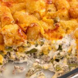 Hamburger Tater Tot Casserole in a baking dish with browned tater tots, melted cheddar cheese, creamy ground beef filling, and green beans visible under the crispy topping.