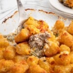 Hamburger Tater Tot Casserole being scooped from a glass baking dish with crispy tater tots, melted cheddar cheese, seasoned ground beef, green beans, and creamy filling.