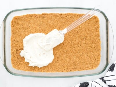 Cream cheese mixture being spread over the graham cracker crust