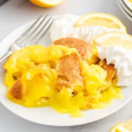 Warm Lemon Cobbler served on a white dessert plate with whipped cream and fresh lemon slices, showcasing the rich lemon filling and golden cobbler topping in this easy homemade dessert recipe.