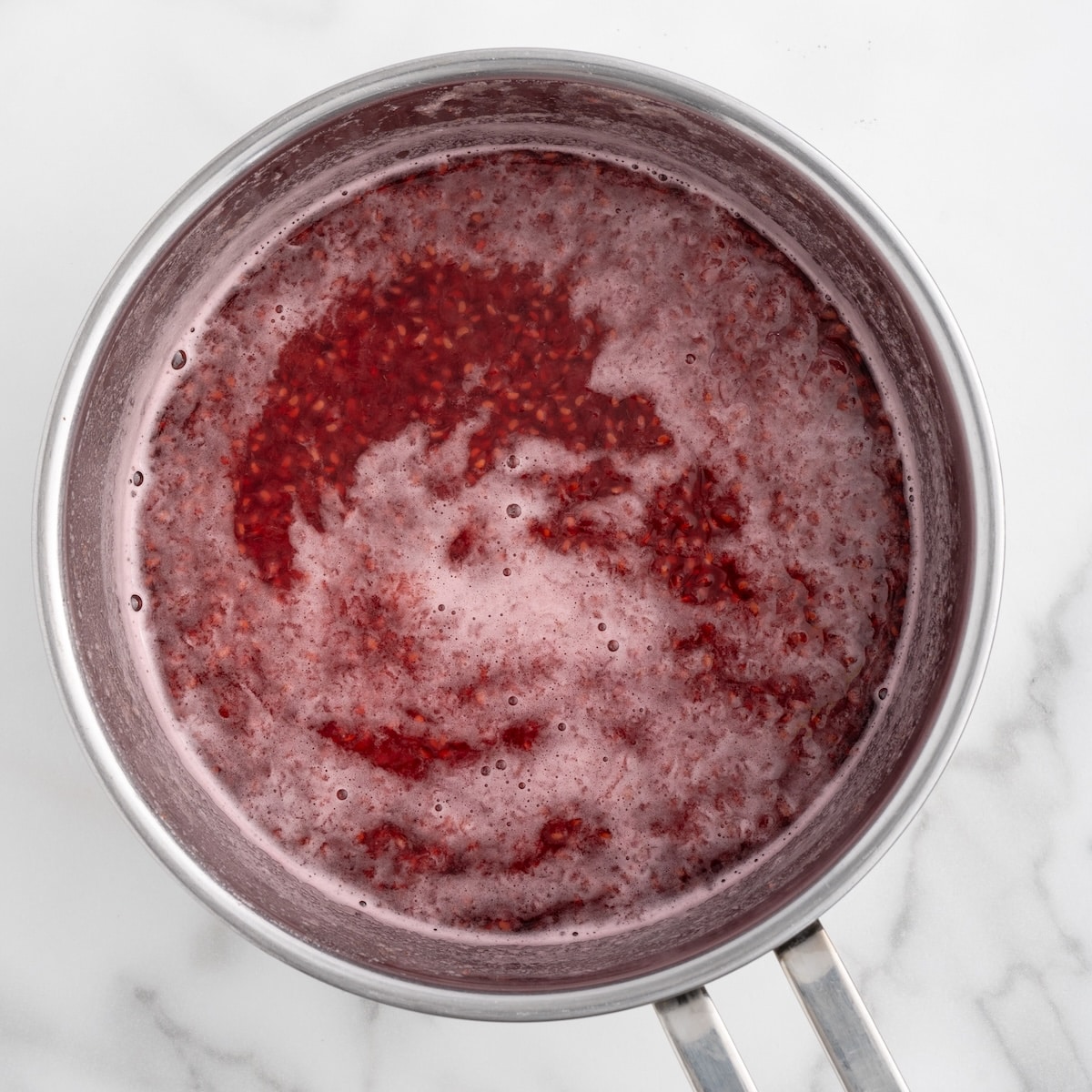 Fresh raspberries simmering in a saucepan with sugar, creating a bubbling raspberry sauce for the tiramisu filling and syrup.