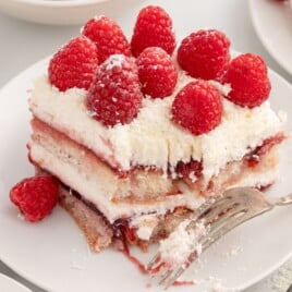 Close-up of Raspberry Tiramisu showing soft ladyfinger layers, raspberry filling, mascarpone cream, fresh raspberries, and white chocolate shavings.