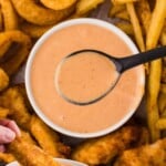 Red Robin Campfire Sauce Pinterest pin with a chicken tender being dipped into the sauce, surrounded by onion rings, fries, and tenders