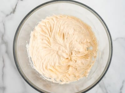 Cream cheese shrimp dip base mixed with seasoning in a clear glass bowl. The creamy mixture has a light pink colour and smooth whipped texture, sitting on a white marble countertop.